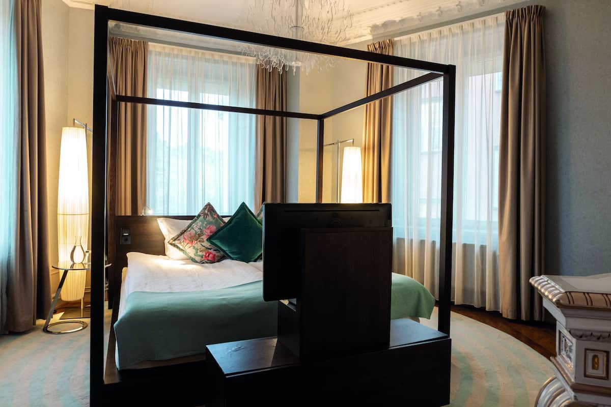 A four-poster bed with a television in front, a bedside table, and a lamp to the left.