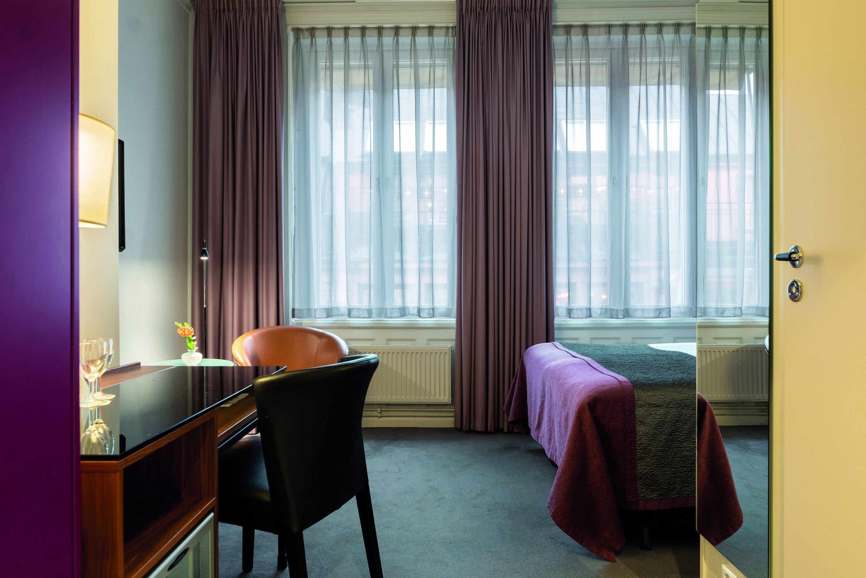 A hotel room with a desk, chair, and a single bed.