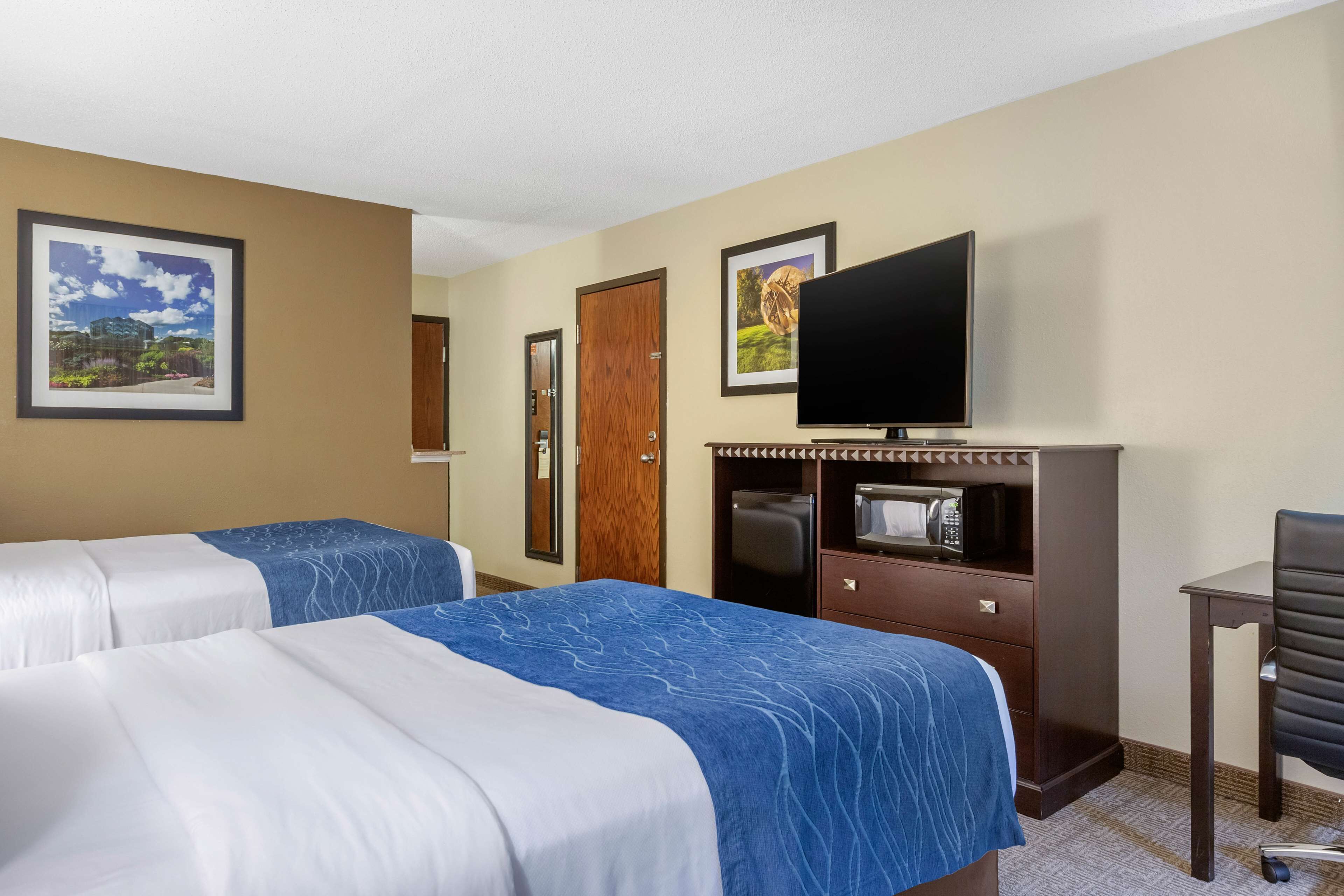 A hotel room with two beds, a television, a desk, and a chair.