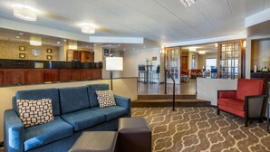 A hotel lobby with a blue sofa, a red chair, a patterned carpet, and a reception desk. - Comfort Inn Grand Rapids Airport (Grand Rapids)