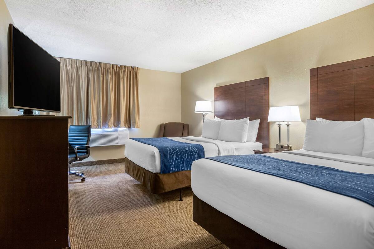 A hotel room with two beds, a desk with a TV, a chair, and a window with curtains.