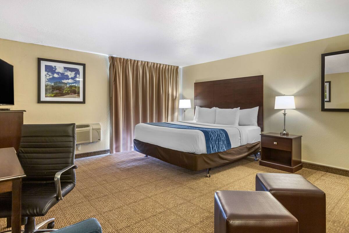 A hotel room with a bed, a desk, a chair, a lamp, and a mirror.