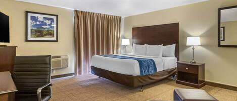 Une chambre d’hôtel avec un lit, un bureau, une chaise, une lampe et un miroir.