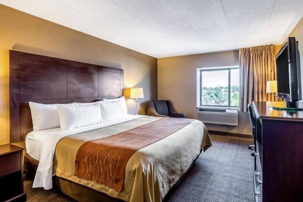 A hotel room with a large bed, a desk with a TV, a chair, and a window with curtains.