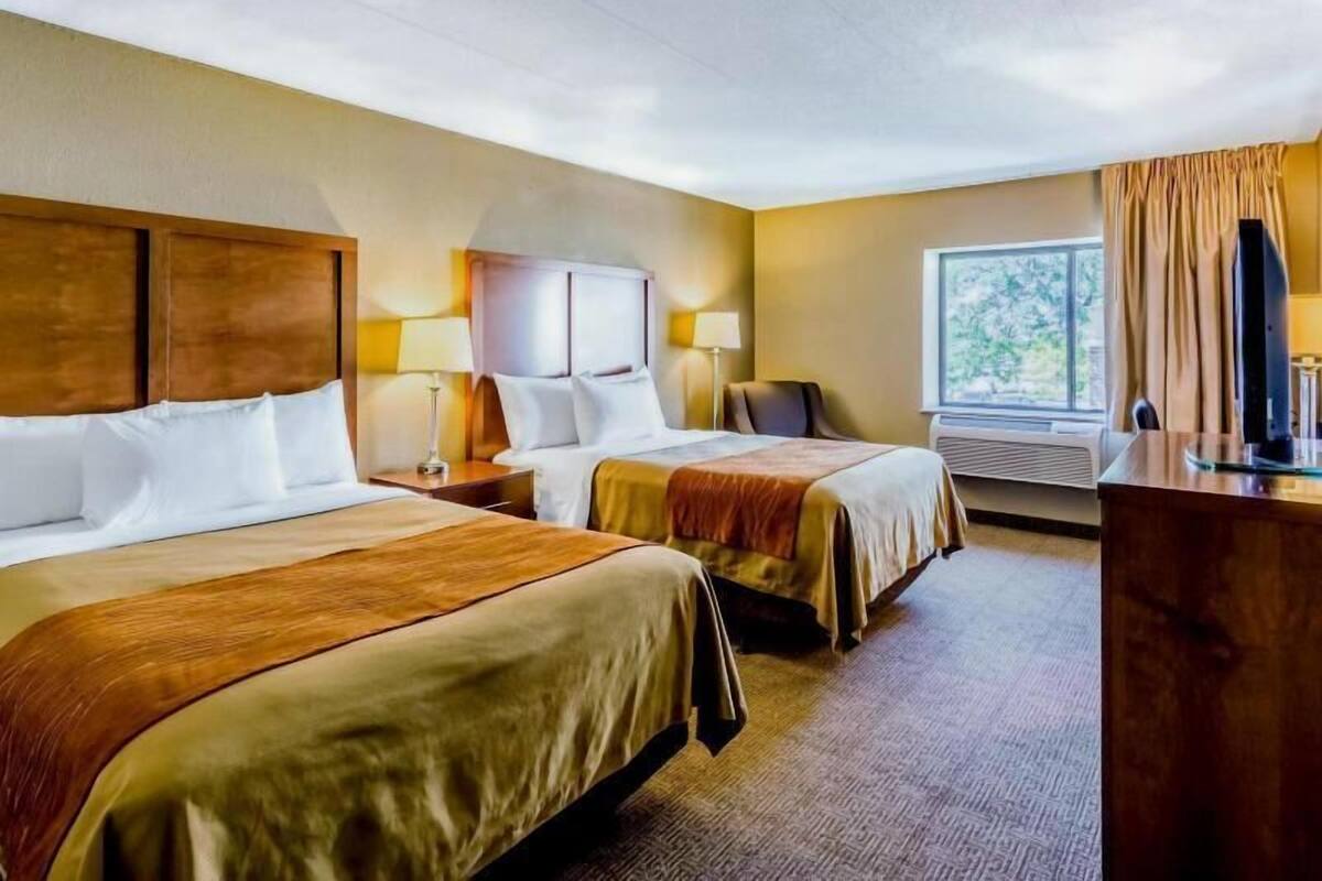 A hotel room with two beds, a desk, a chair, a television, and a window with curtains.