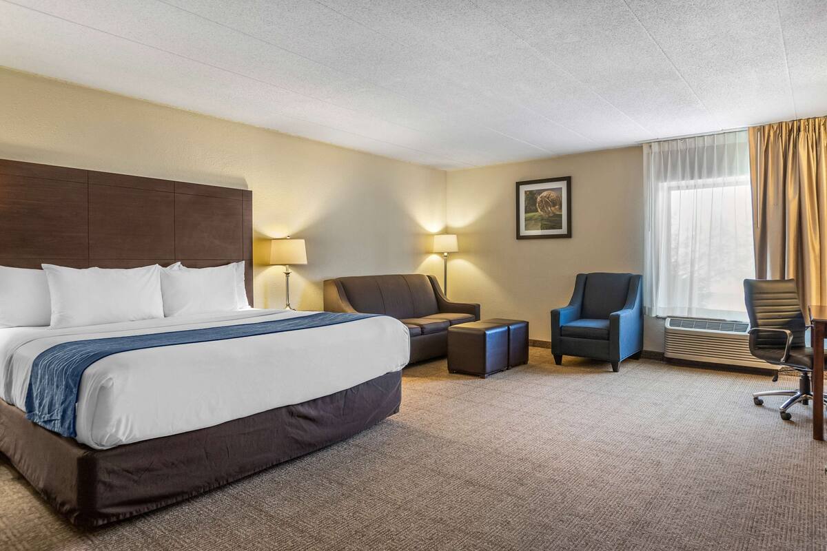 A hotel room with a large bed, two armchairs, a small table, and a desk with a chair.