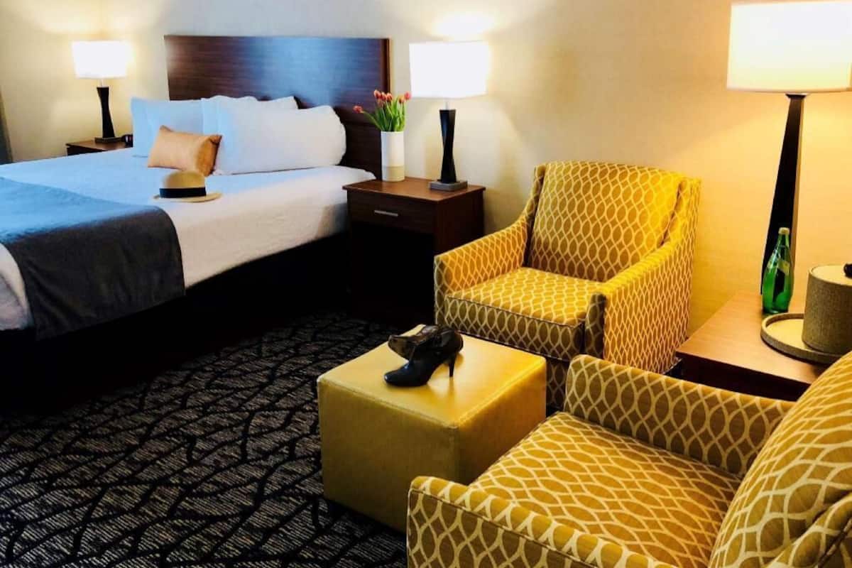 A hotel room with a bed, two nightstands with lamps, a sofa, a chair, and a small ottoman.