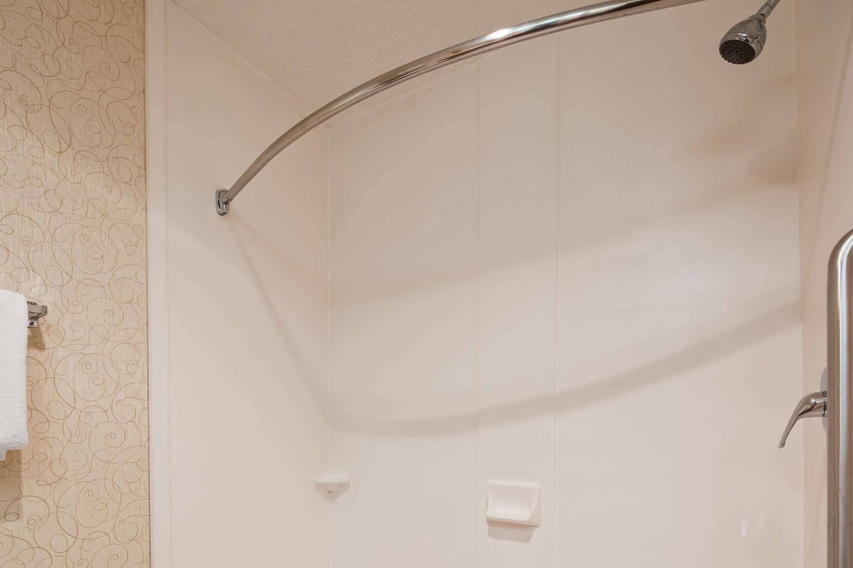 Una ducha con estructura metálica curva, una toalla blanca en un perchero y un jabonera en la pared.