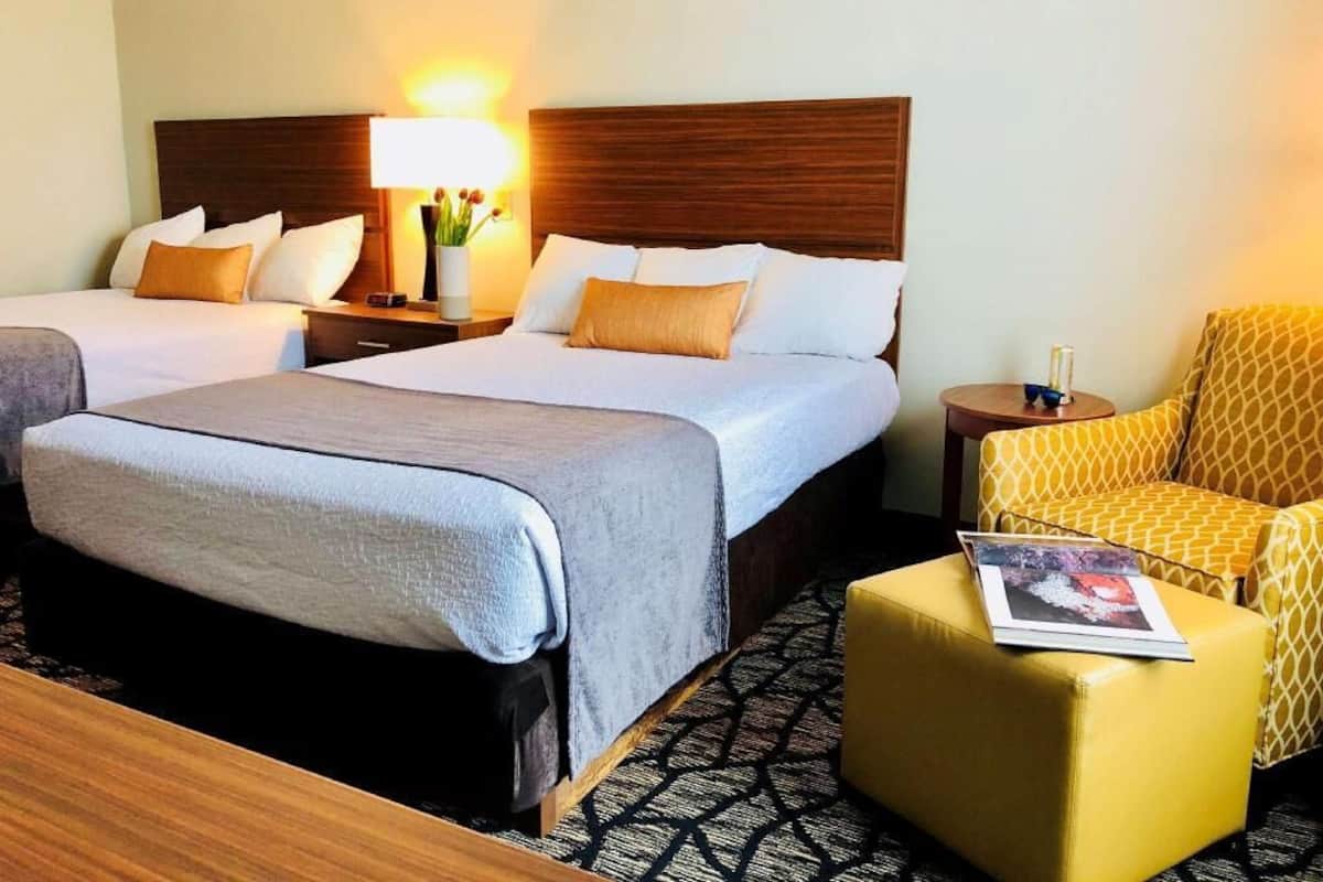 A hotel room with two beds, a small table, a chair, and a lamp.
