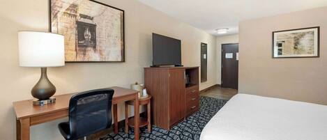 Ein Hotelzimmer mit Bett, Schreibtisch, Stuhl, Fernseher und Bildern an den Wänden.