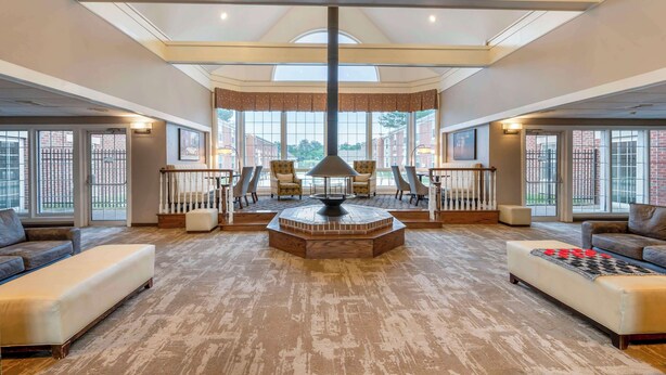 A spacious living room with a central fireplace, large windows, and a view of the outside. - Best Western Westminster Hotel (Westminster)