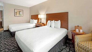 A hotel room with two beds, a bedside table with a lamp, a small side table with toiletries, and a patterned rug. - Best Western Westminster Hotel (Westminster)