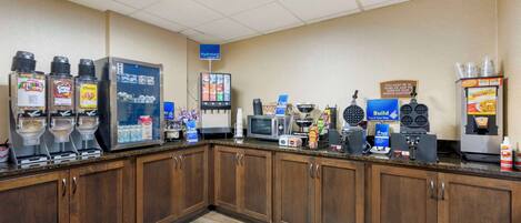 A self-service breakfast area with beverage dispensers, a microwave, and a waffle maker.