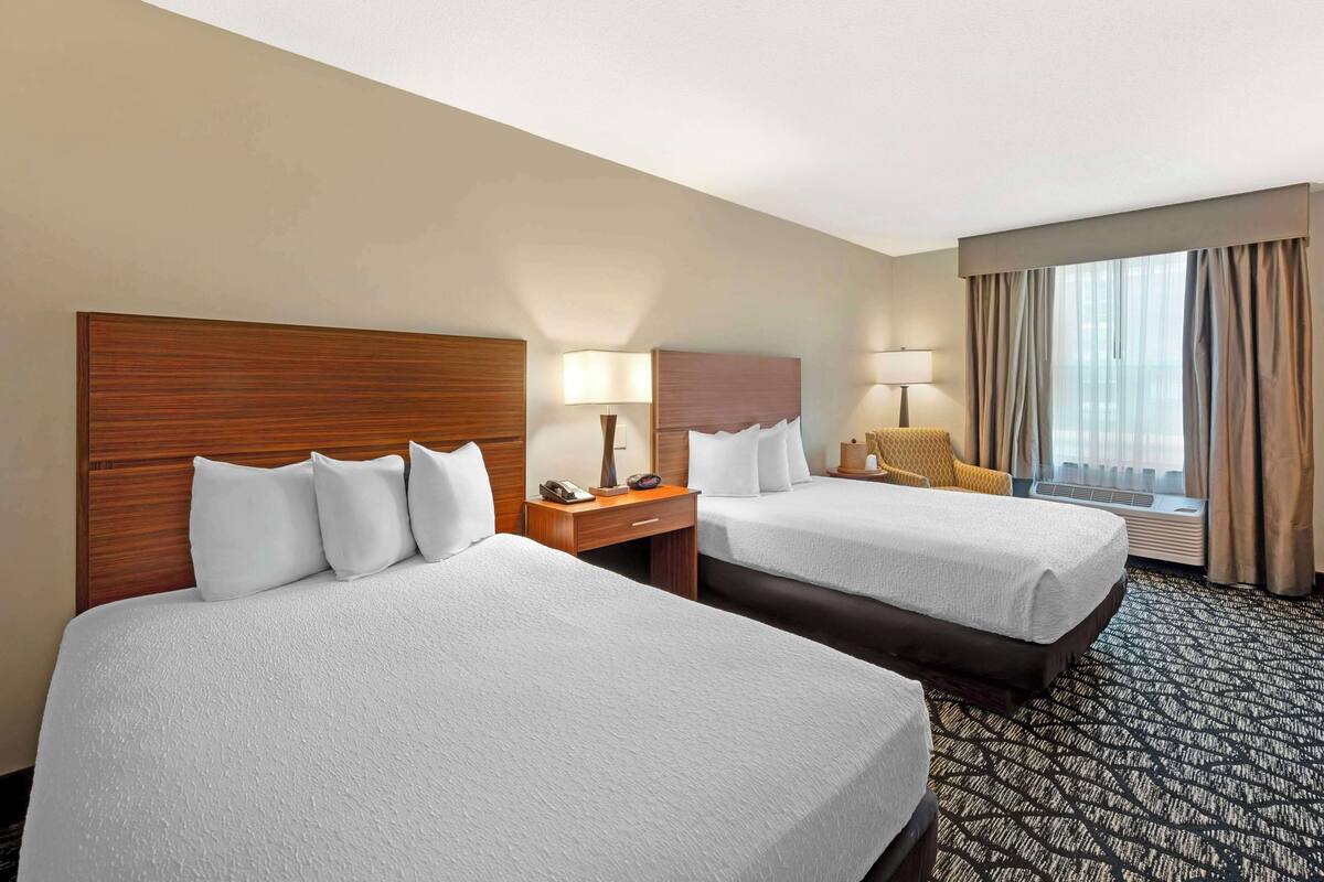 A hotel room with two beds, a desk, a chair, a lamp, and a window with curtains.