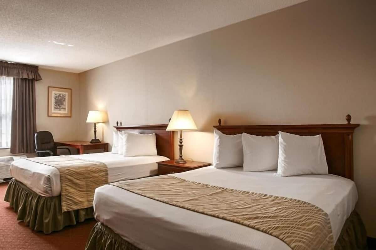 A hotel room with two beds, a desk, a chair, and two lamps.