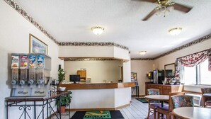 A hotel lobby with a reception desk, a coffee machine, and a dining area with chairs and a table.