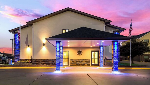 A hotel entrance with a covered patio, American flags, and a sunset sky.