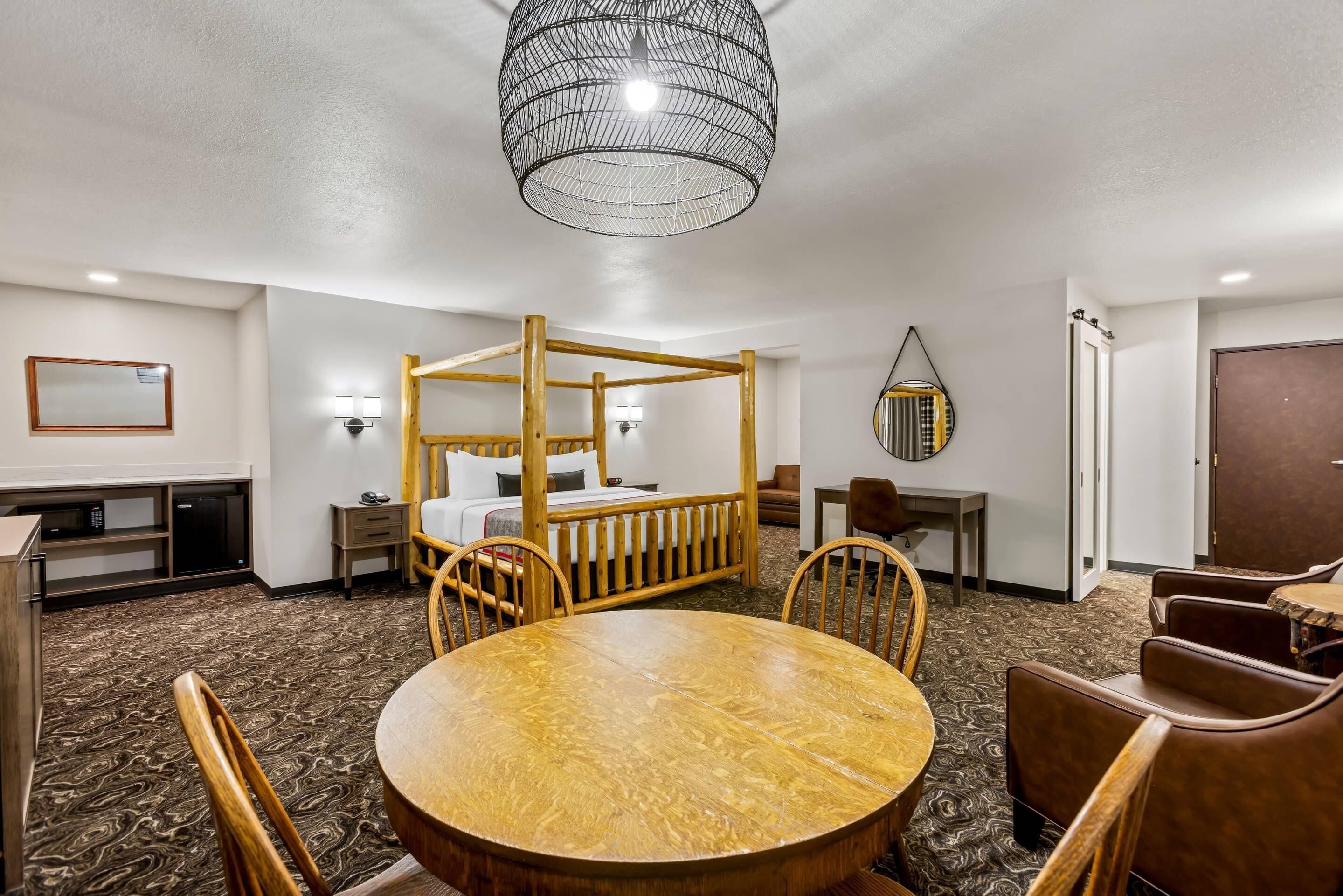 Una habitación de hotel con una cama con dosel de madera, una mesa redonda de comedor y un espejo grande.
