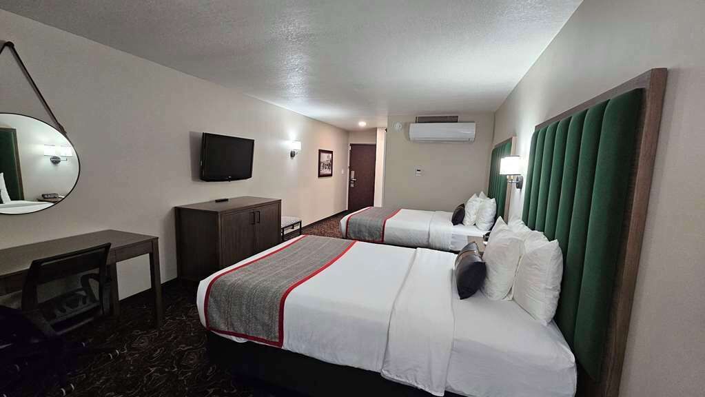 Een hotelkamer met twee bedden, een bureau, een televisie en een spiegel.