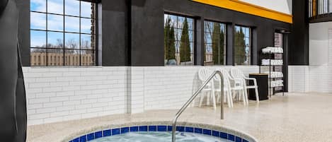 A modern indoor pool area with a hot tub, white tiled walls, and a yellow accent wall.