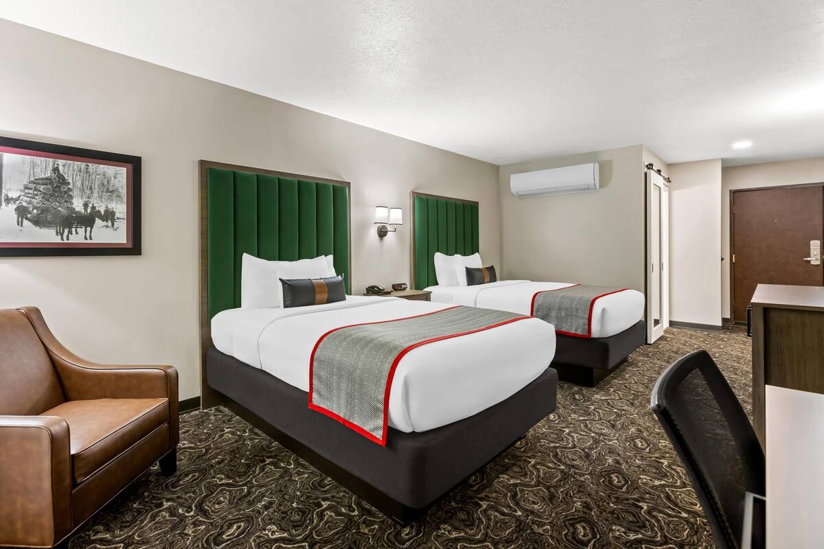 A hotel room with two beds, a desk, a chair, and a framed picture on the wall.