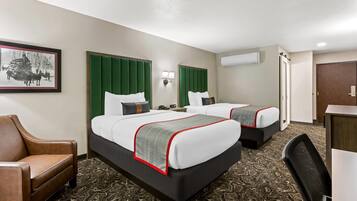 A hotel room with two beds, a desk, a chair, and a framed picture on the wall.