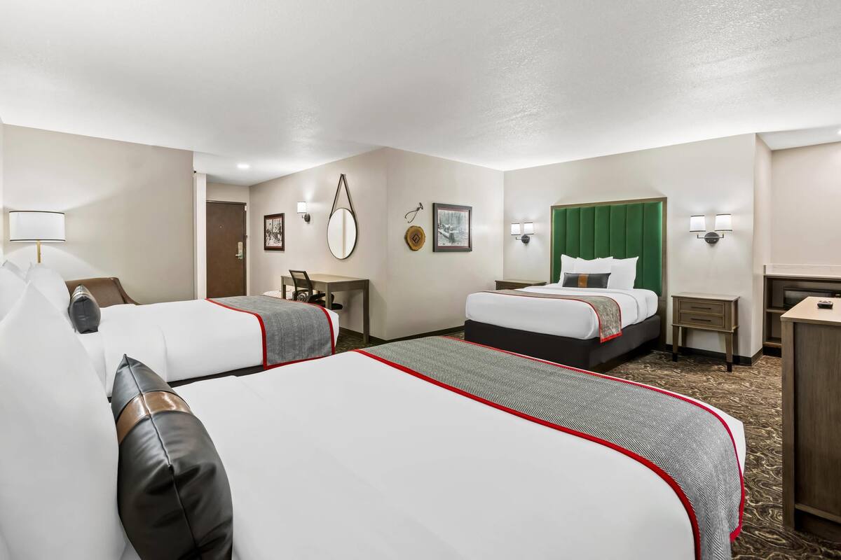 A hotel room with two beds, a desk, a chair, a mirror, and wall-mounted lights.