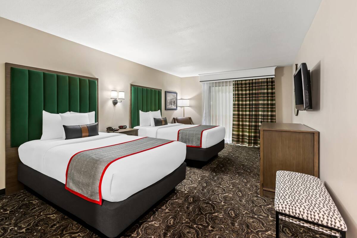 A hotel room with two beds, a desk, a chair, a TV, and a patterned carpet.