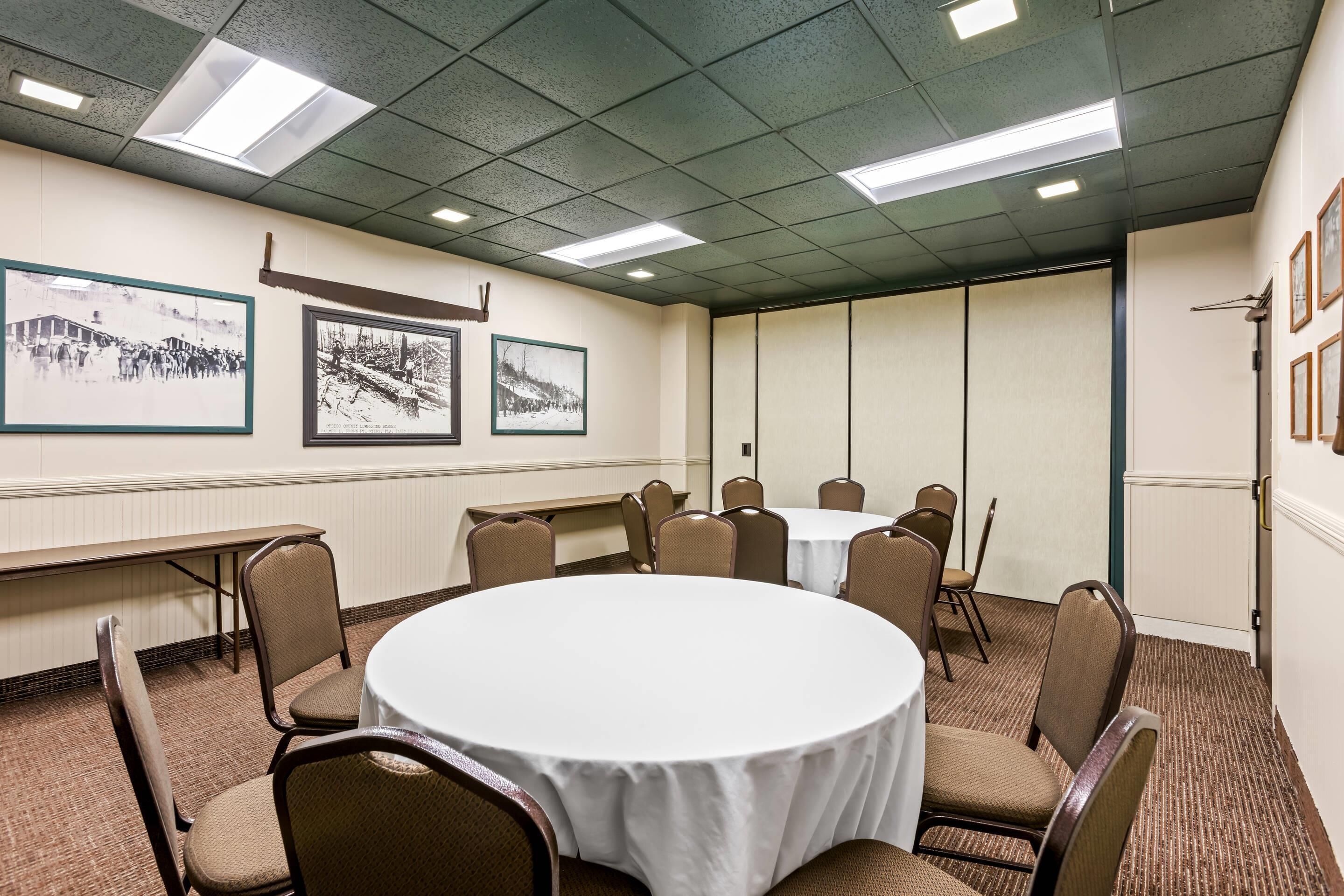 A conference room with a round table, chairs, framed pictures on the wall, and a carpeted floor.