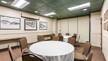 A conference room with a round table, chairs, framed pictures on the wall, and a carpeted floor.