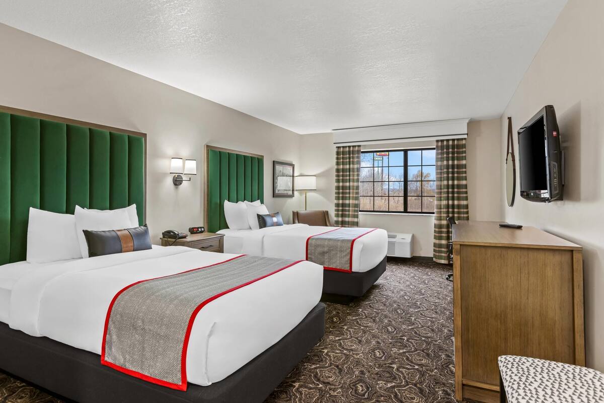 A hotel room with two beds, a desk, a TV, and a window with curtains.
