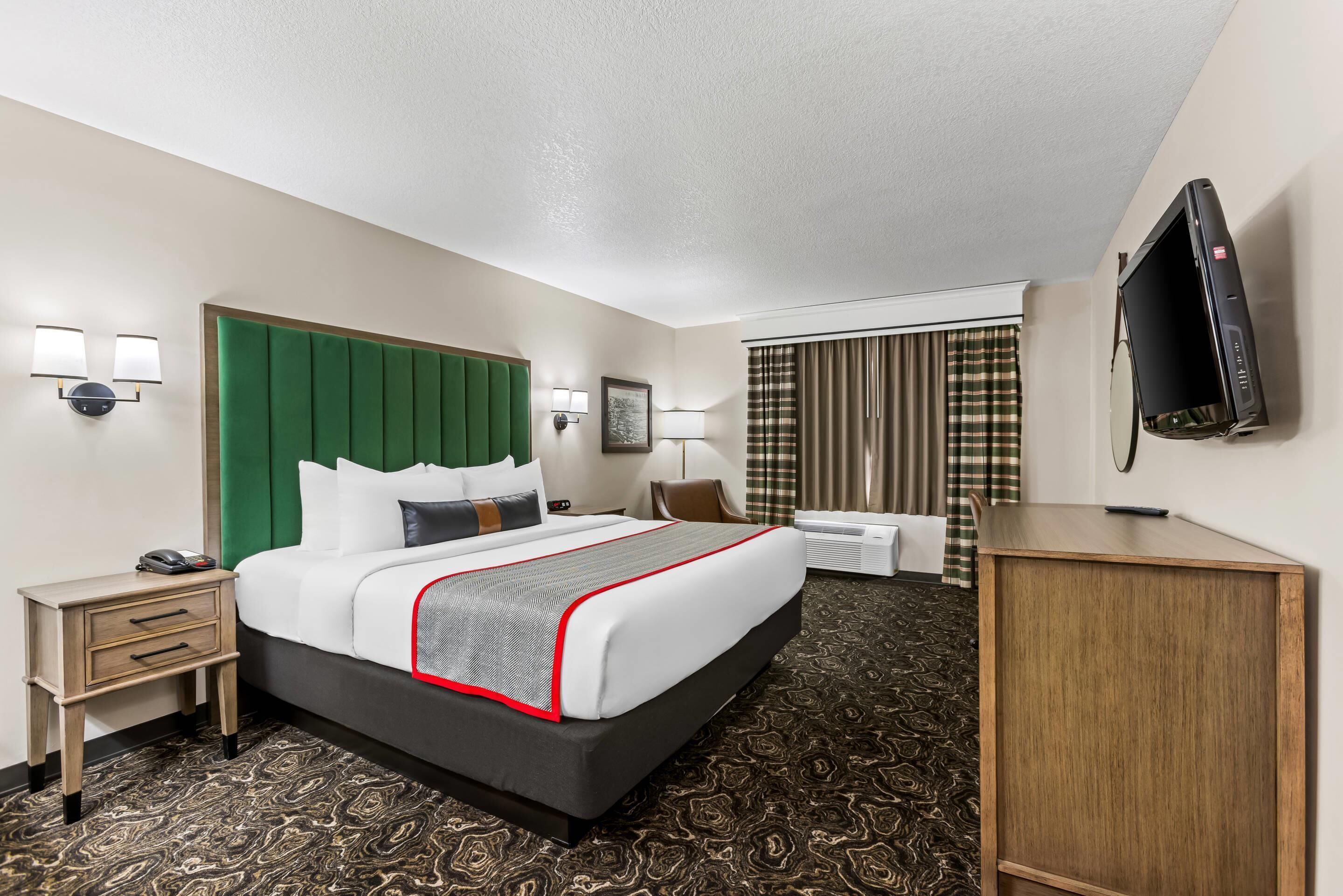 A hotel room with a large bed, a desk, a chair, a TV, and a small table.