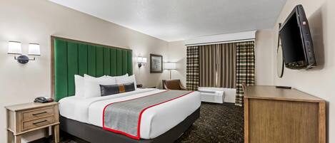 A hotel room with a large bed, a desk, a chair, a TV, and a small table.