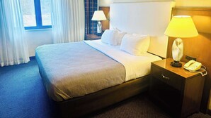 Een hotelkamer met een groot bed, een nachtkastje met een lamp, een telefoon en een raam met gordijnen.