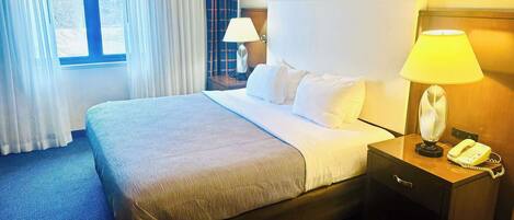 Ein Hotelzimmer mit einem großen Bett, einem Nachttisch mit Lampe, einem Telefon und einem Fenster mit Vorhängen.