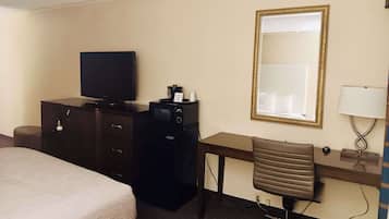 Camera d'albergo con un letto, una scrivania con sedia, una televisione, un minibar e uno specchio grande.