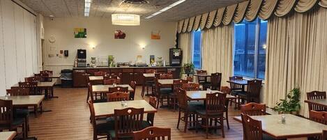 A spacious dining area with multiple tables and chairs, a chandelier, and large windows with curtains.
