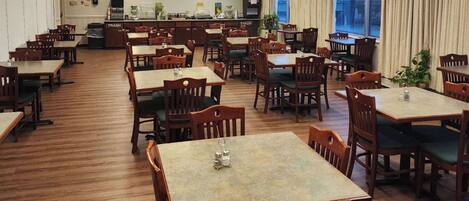 A spacious dining area with multiple wooden tables and chairs, a trash bin, and a counter with various items.