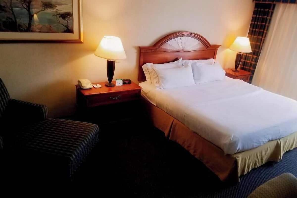 A hotel room with a bed, two bedside tables with lamps, a chair, and a painting on the wall.