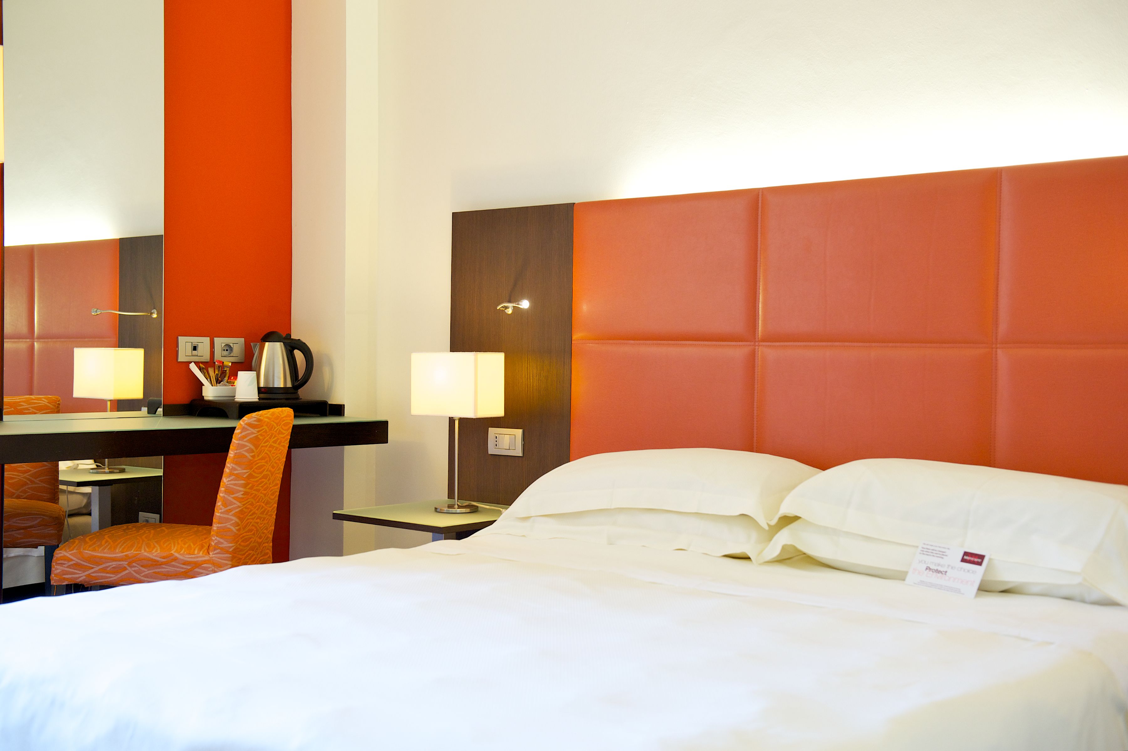 A hotel room with a bed, a desk, a chair, a lamp, and a mirror.