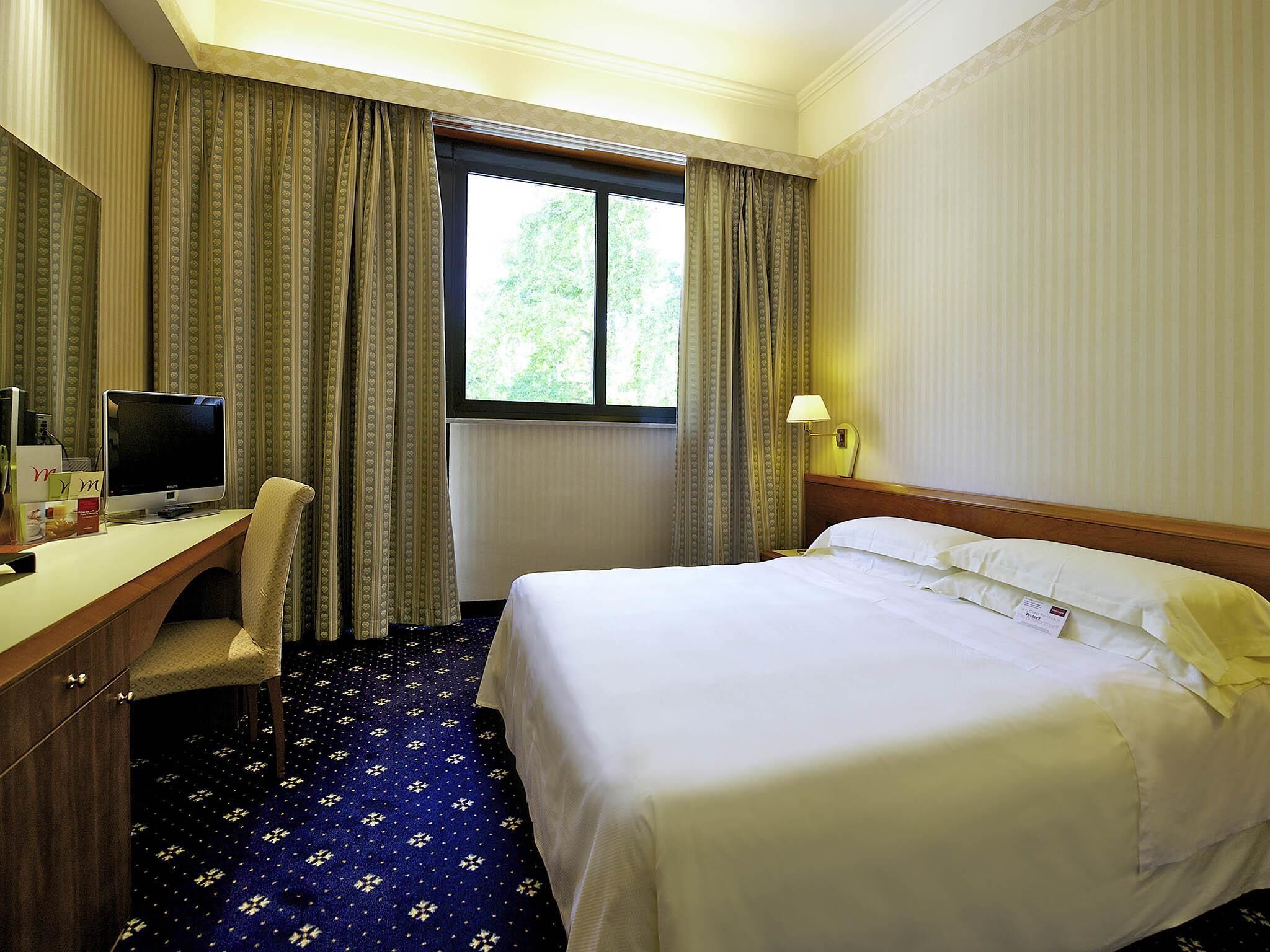A hotel room with a bed, desk, chair, television, and window with curtains.