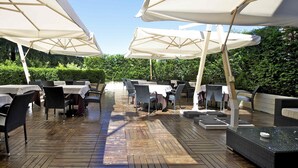 An outdoor patio with tables and chairs under large umbrellas, surrounded by greenery. - Mercure Astoria Reggio Emilia (Reggio nell'Emilia)