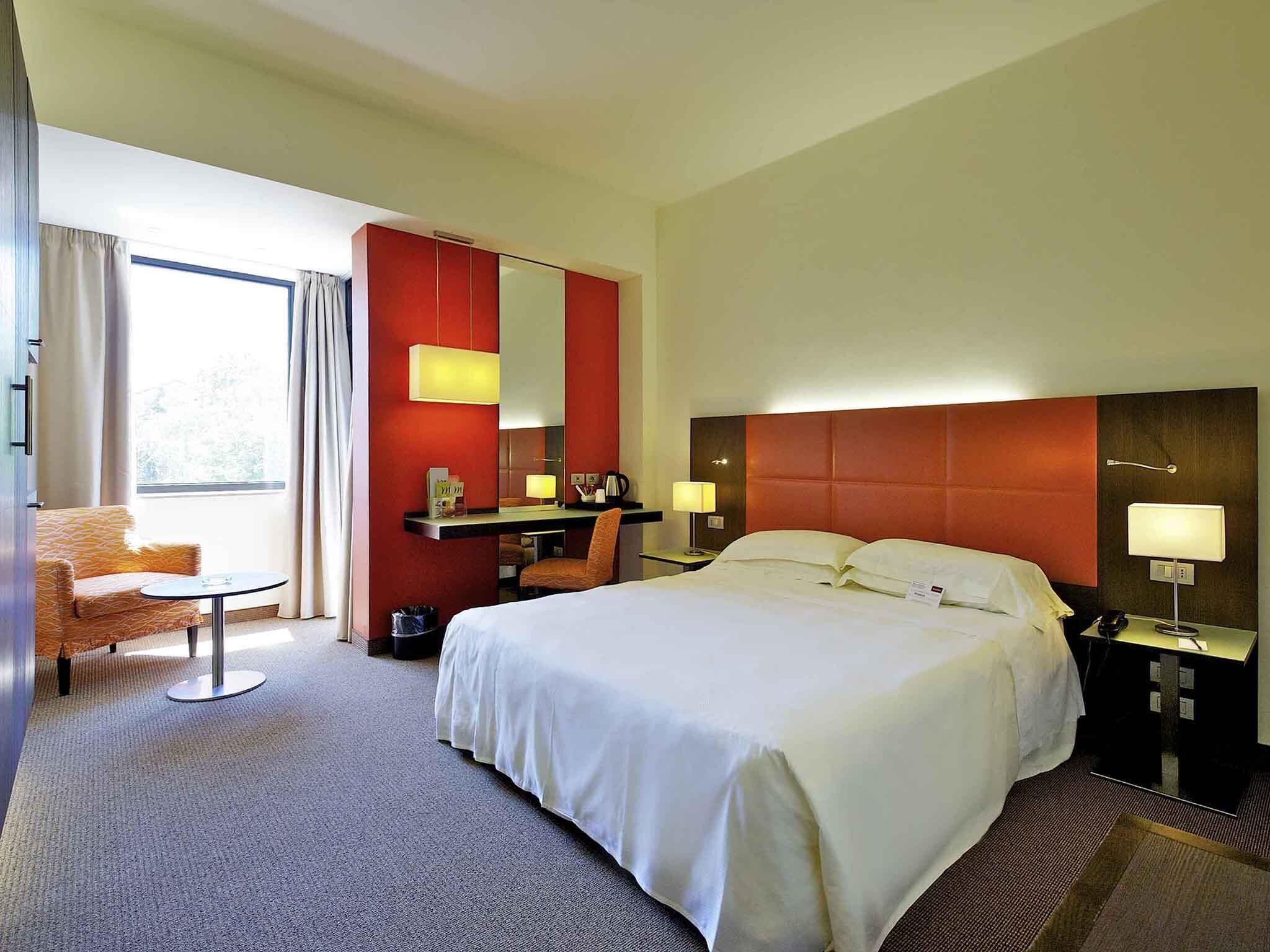 Una camera d'albergo con un letto grande, una scrivania, una sedia e una finestra.