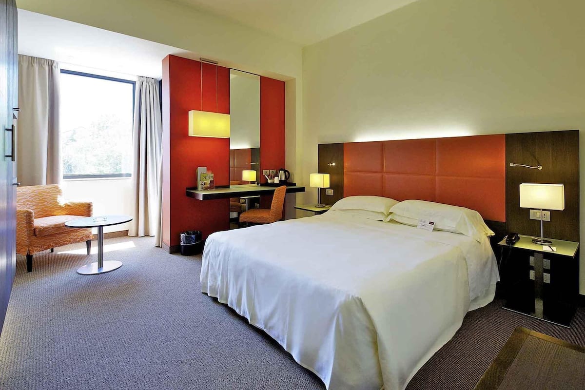 Ein Hotelzimmer mit einem großen Bett, einem Schreibtisch, einem Stuhl und einem Fenster.