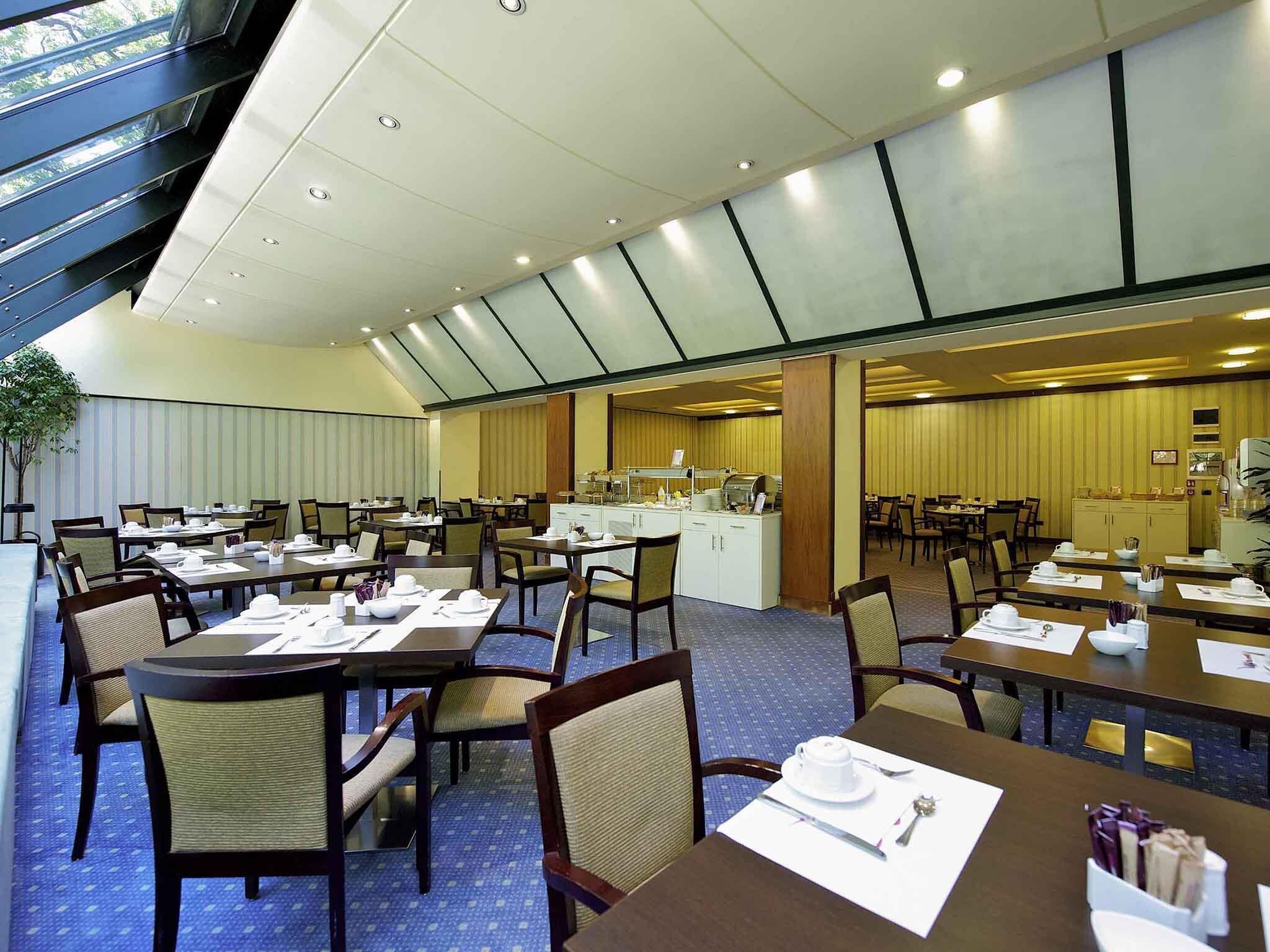 Ein großzügiger Hotel-Speisesaal mit mehreren Tischen und Stühlen, einer Buffet-Anrichtung und einem großen Fenster, das für natürliches Licht sorgt.