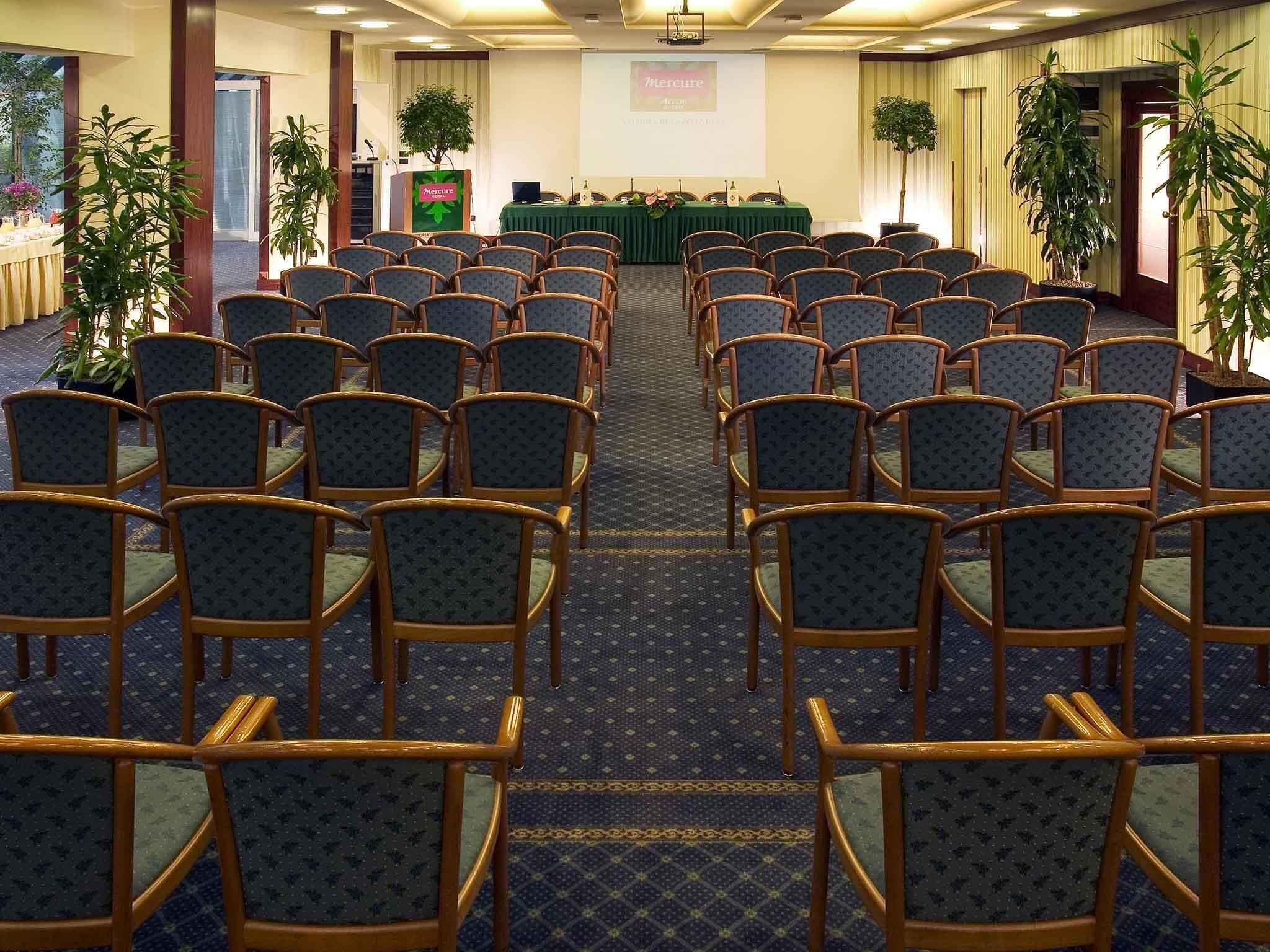 A conference room with rows of chairs, a podium, and a presentation screen.