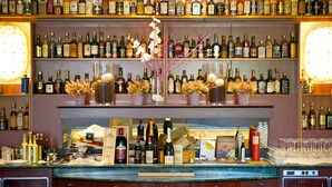 A bar with shelves stocked with various bottles of alcohol, a display of wine glasses, and decorative flowers. - Mercure Astoria Reggio Emilia (Reggio nell'Emilia)