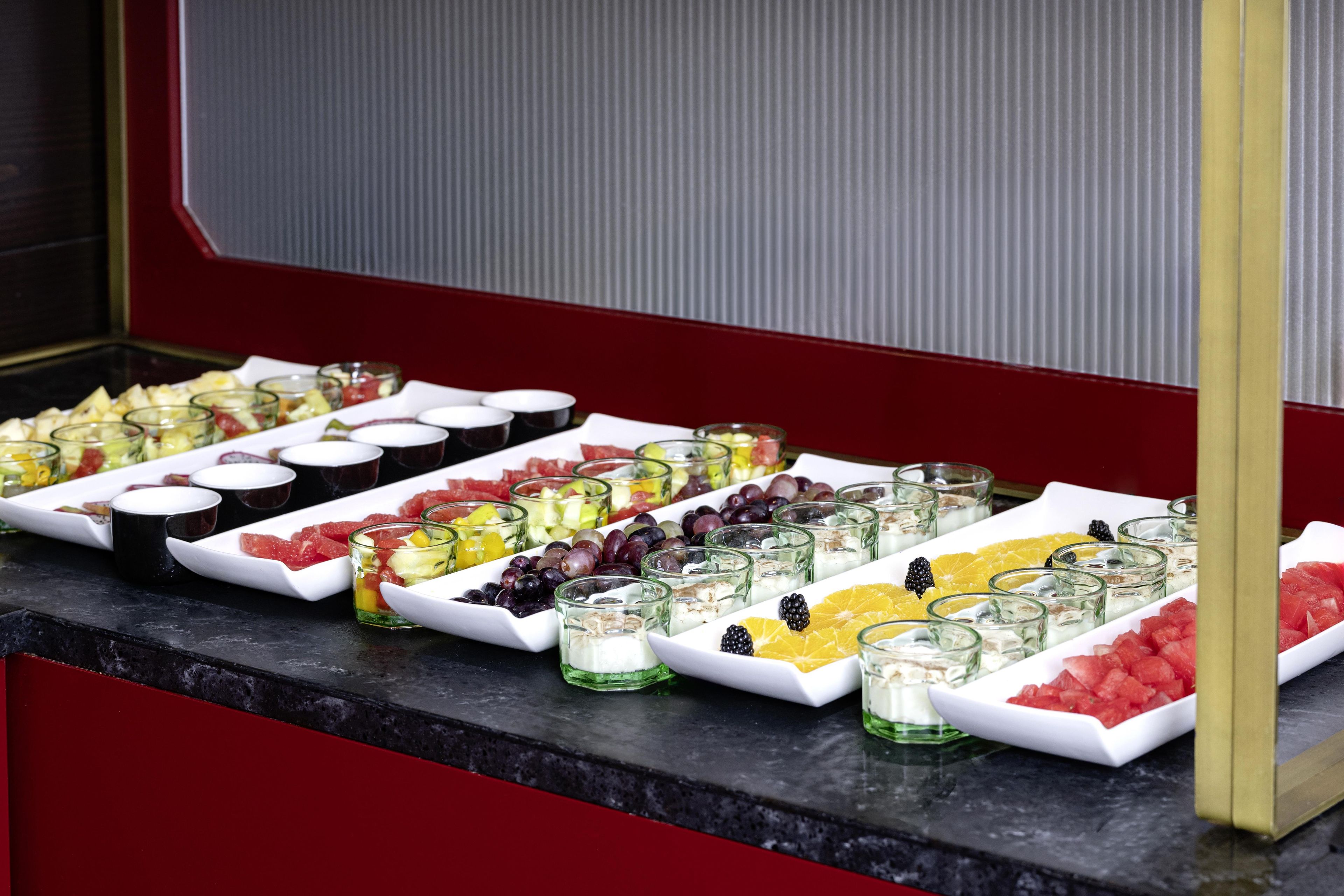 Un bufé con diversas frutas y postres dispuestos en bandejas blancas.