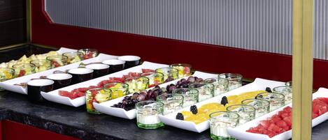 Un bufé con diversas frutas y postres dispuestos en bandejas blancas.