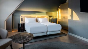 A modern bedroom with a bed, a chair, a small table, and a TV on the wall.